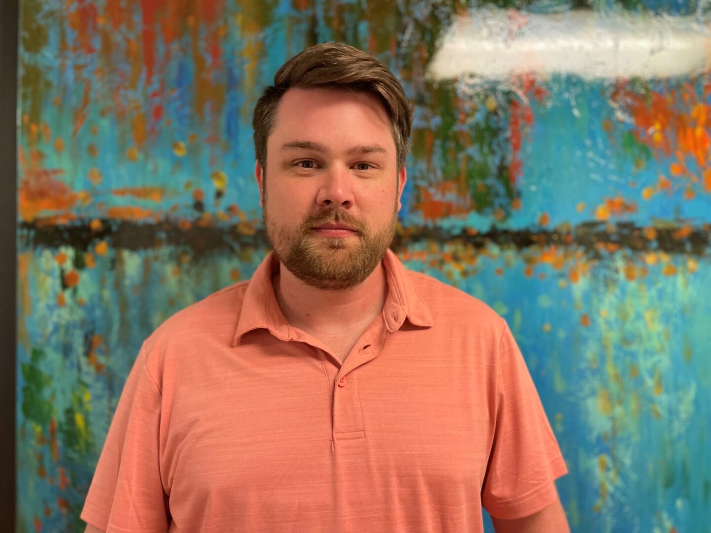 Travis Baker stands in front of a blue and orange painting